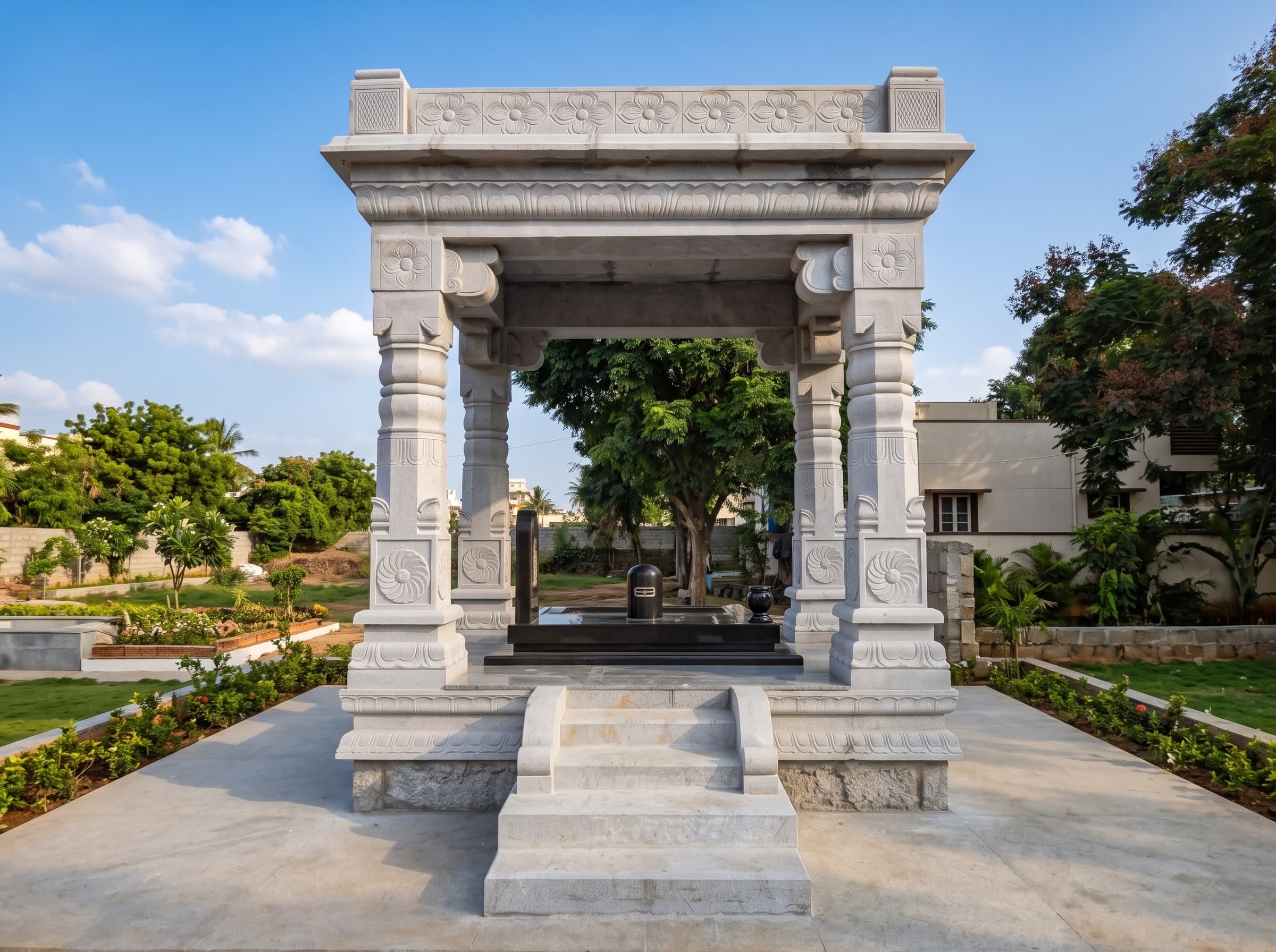 White carved granite mandapam over a black granite memorial in a garden