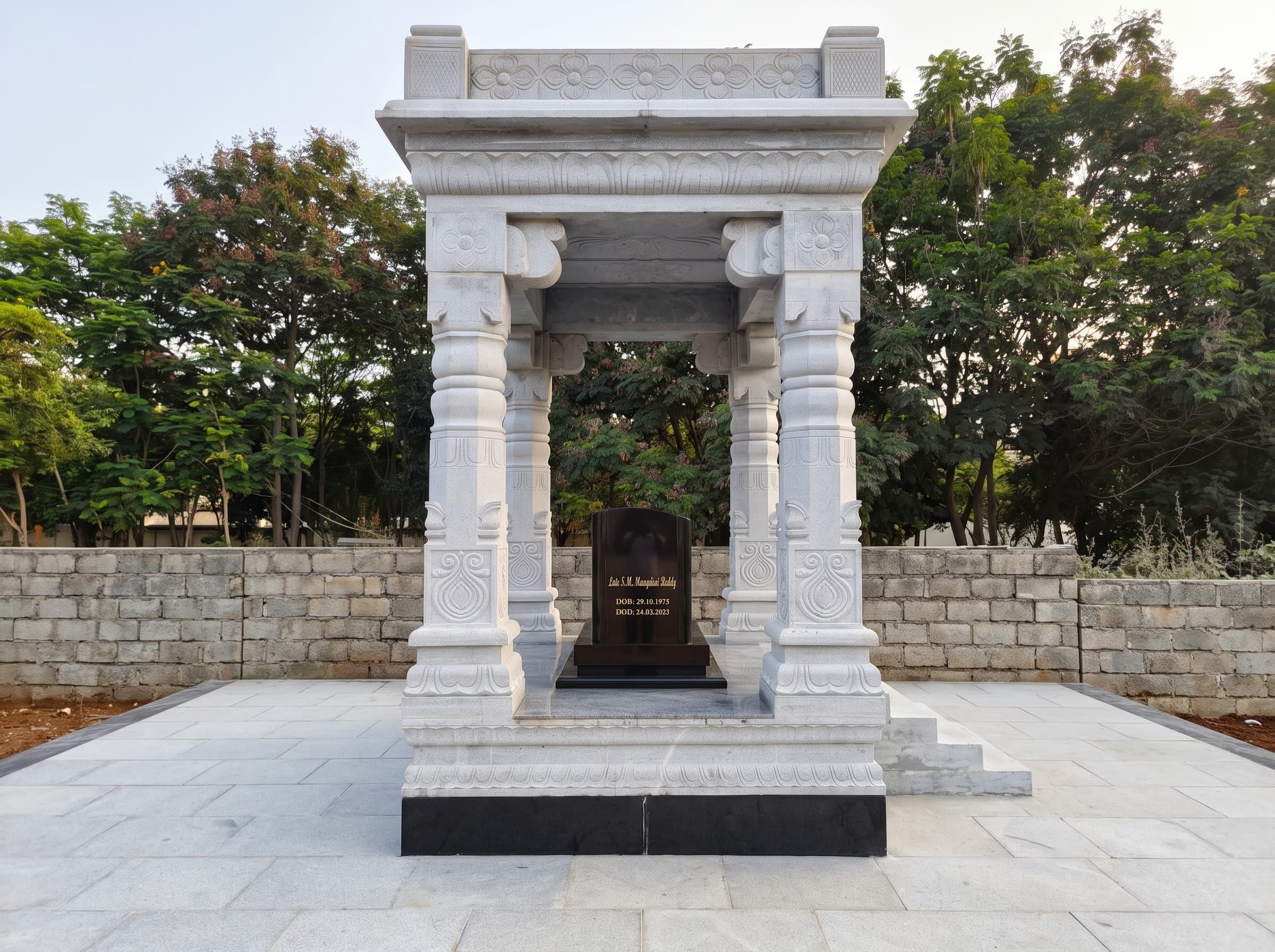 White marble mandapam structure sheltering a black granite memorial